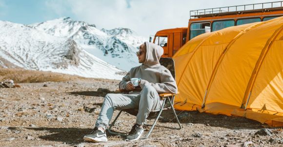 Tranquil Escapes - Full length of male camper sitting on folding chair next to tent in middle of mountain valley and enjoying views